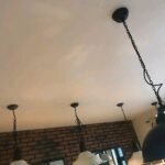 Plafond blanc repeint, luminaires suspendus et mur de briques, chantier à Montpellier